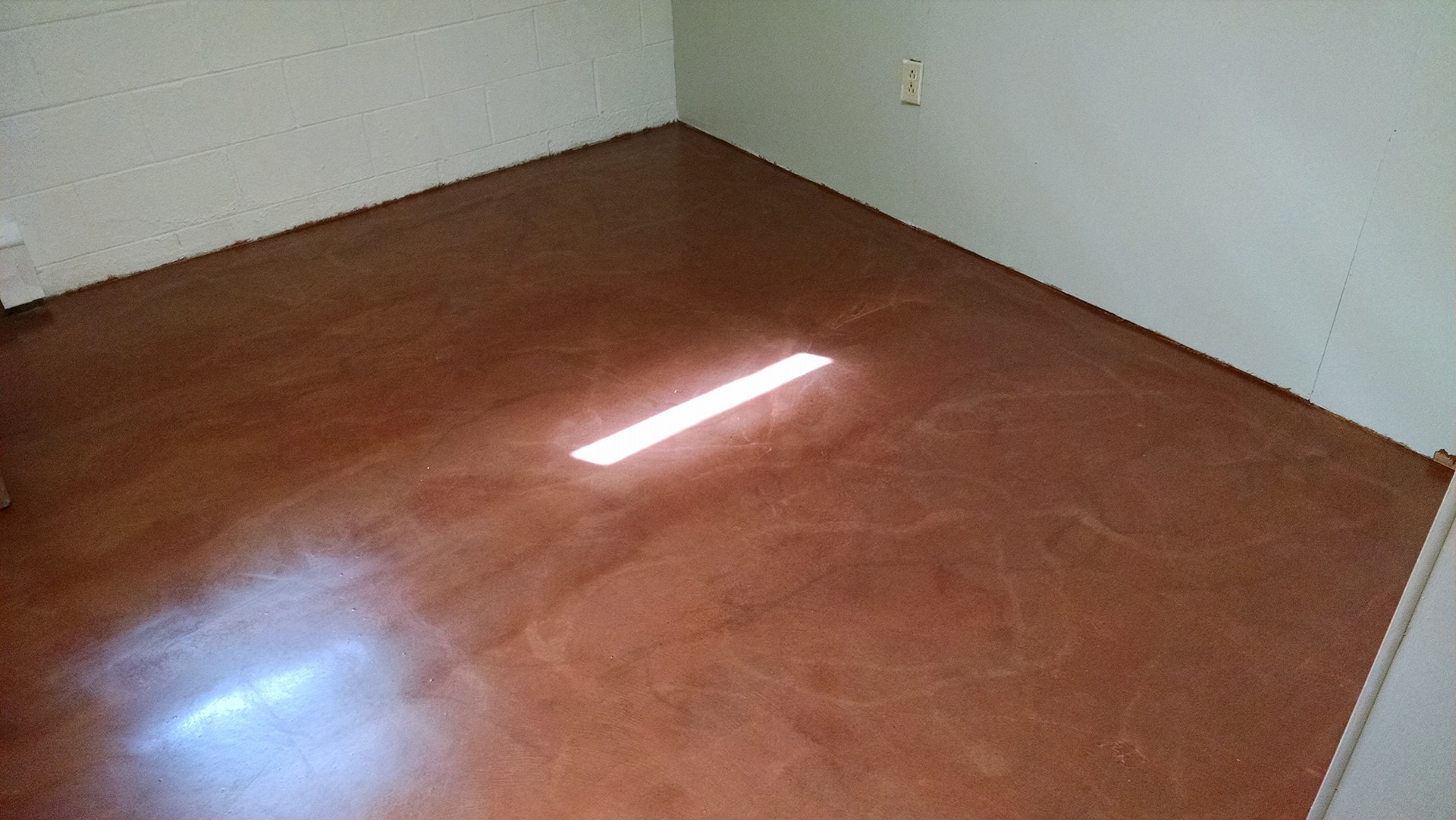 Brown, glossy floor in a room with white walls, illuminated by sunlight.