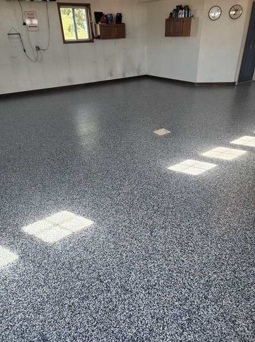Epoxy-coated garage floor with flecks. Sunlight casts square shadows. White walls, window, and small shelves.