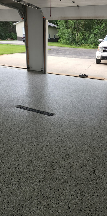 Garage interior with a speckled floor and a car parked outside.