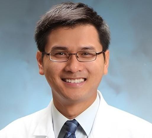 A smiling man wearing glasses and a white coat and tie