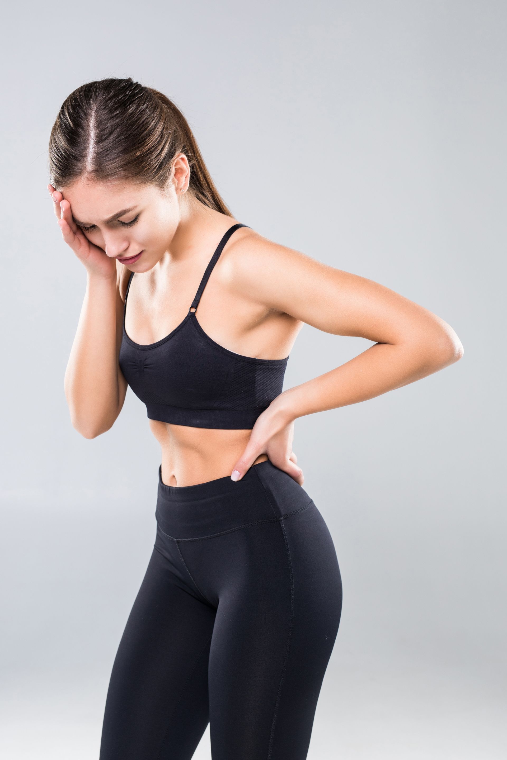 A woman in a sports bra and leggings is holding her back in pain.
