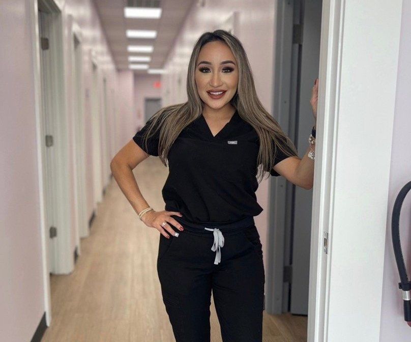 A woman in scrubs is standing in a hallway with her hands on her hips.