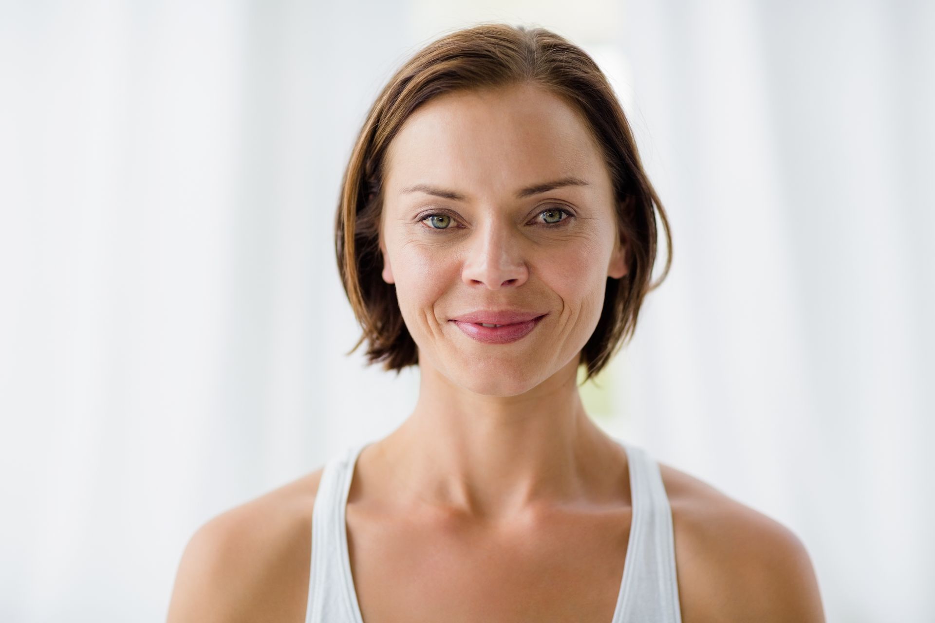 A woman in a white tank top is smiling and looking at the camera.