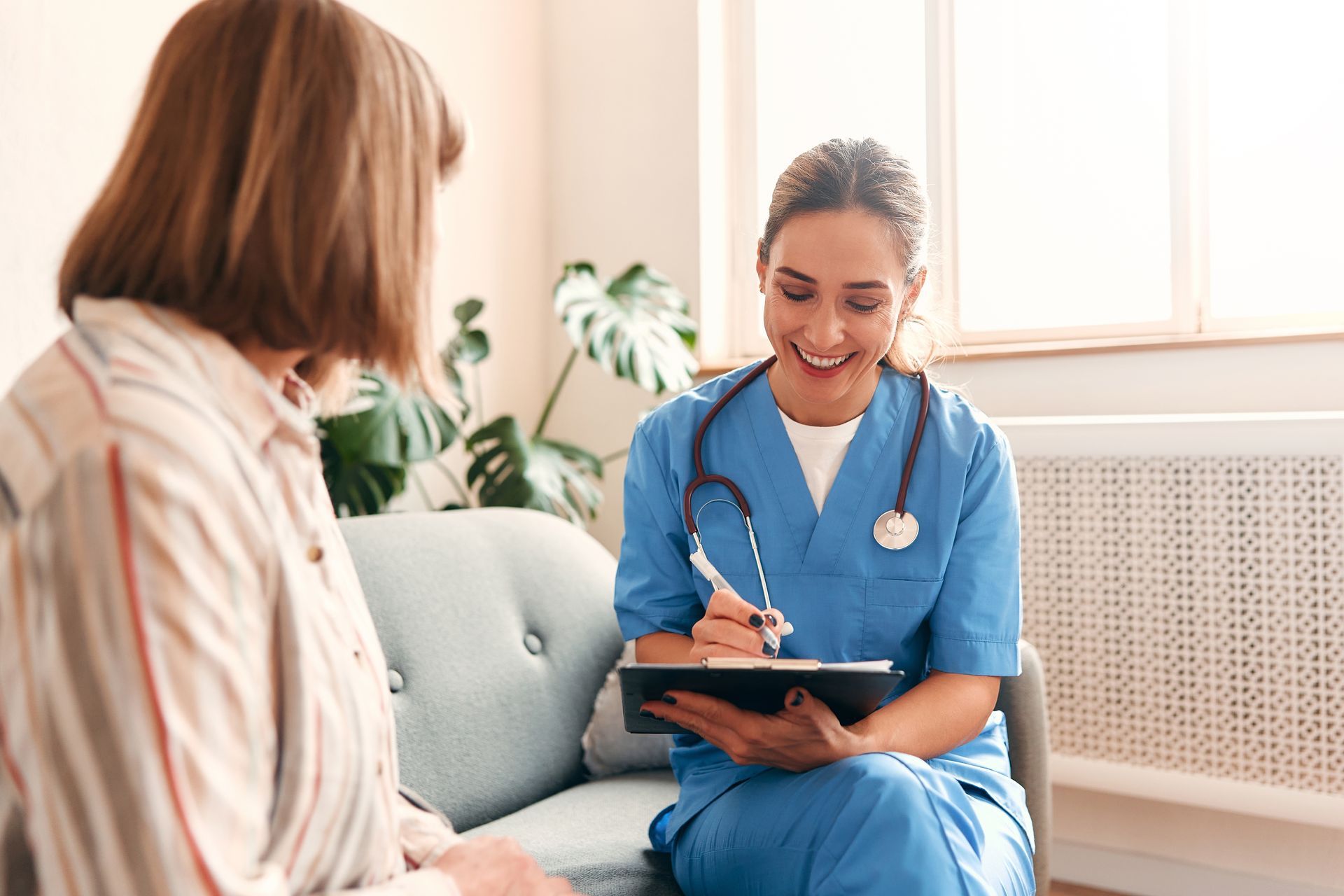 A nurse is sitting on a couch talking to a patient.