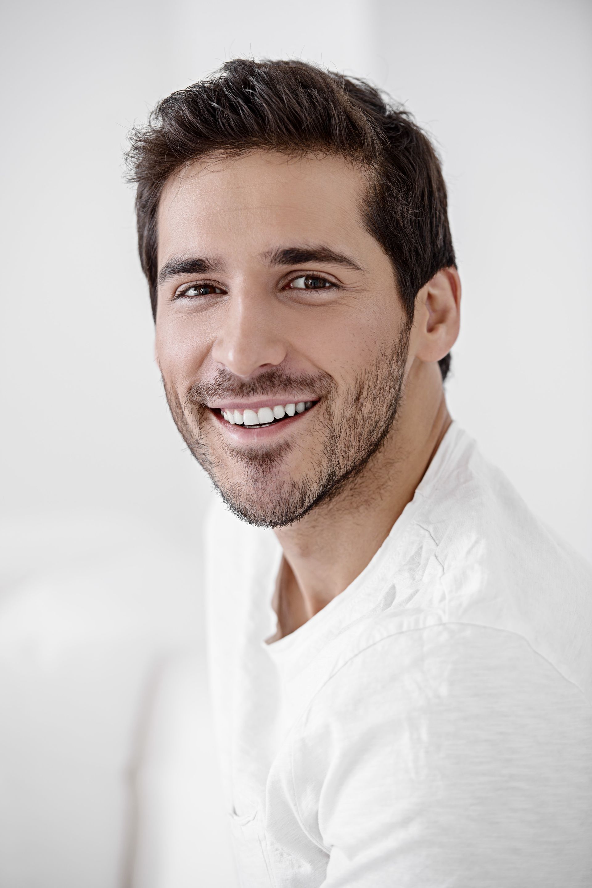 A man with a beard is smiling for the camera while wearing a white shirt.
