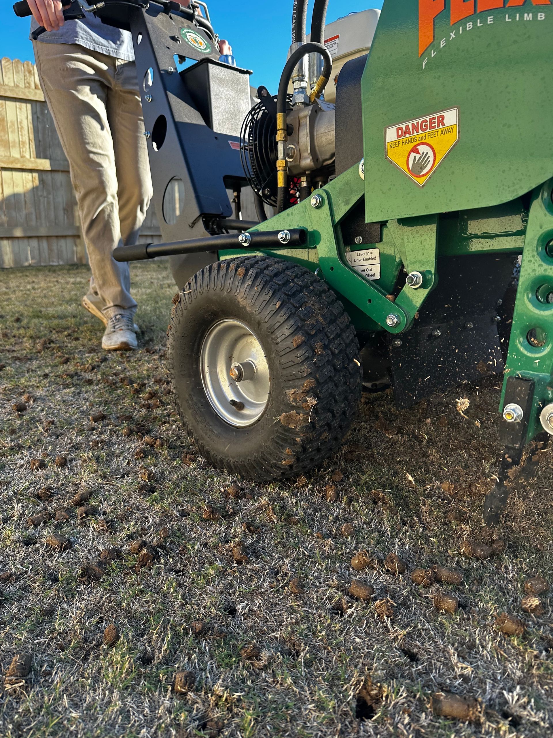 Person standing beside a green core aerator on grass