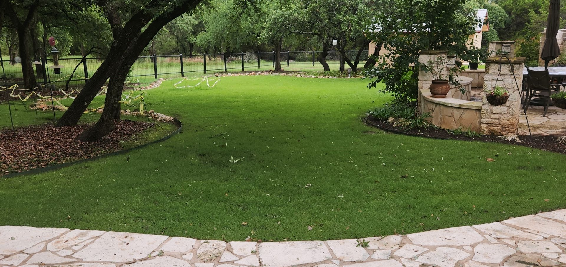 Tree-shaded park lawn with bright green grass, stone edging, and a paved path in front