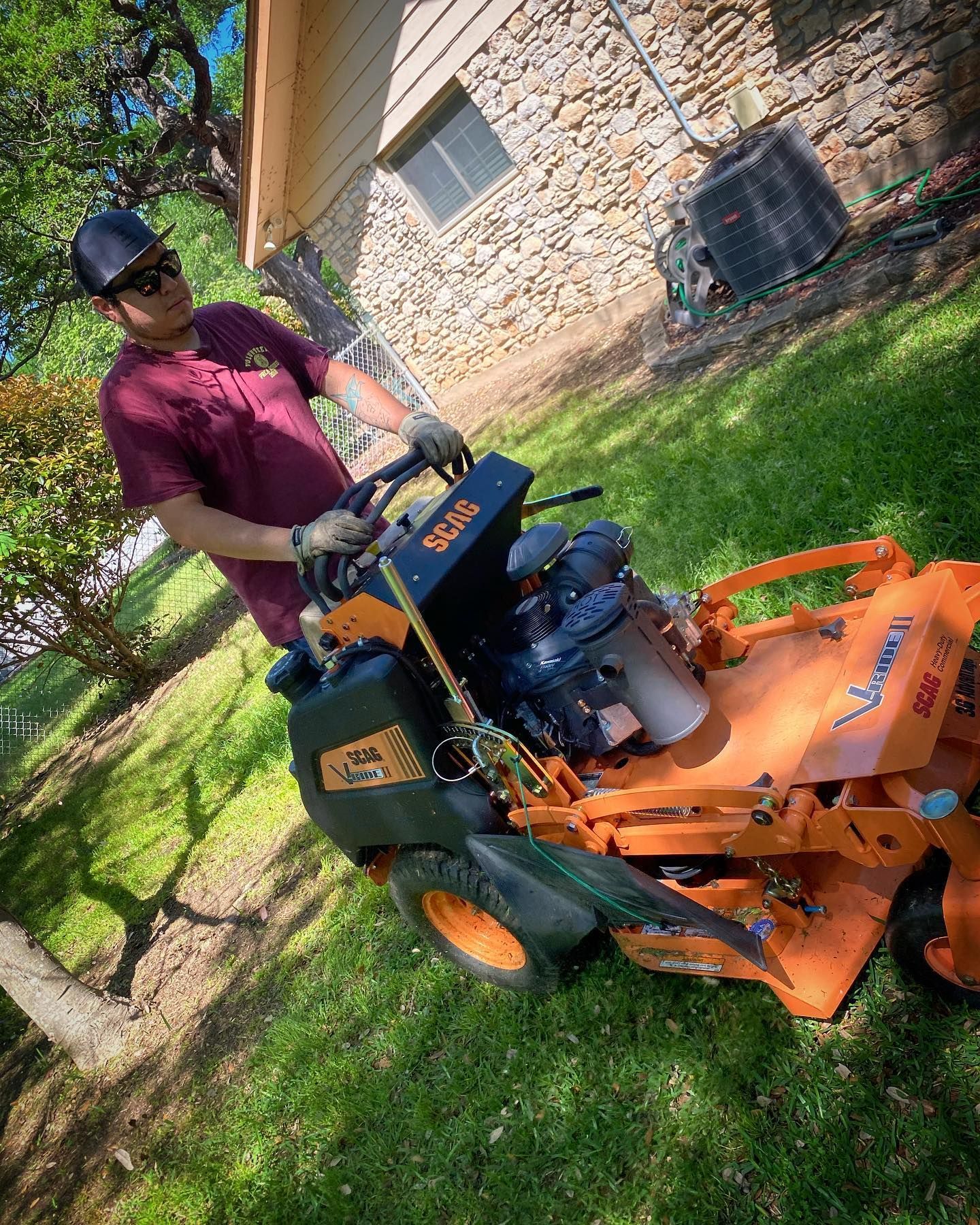 Person mowing grass on an orange riding mower beside a brick building.