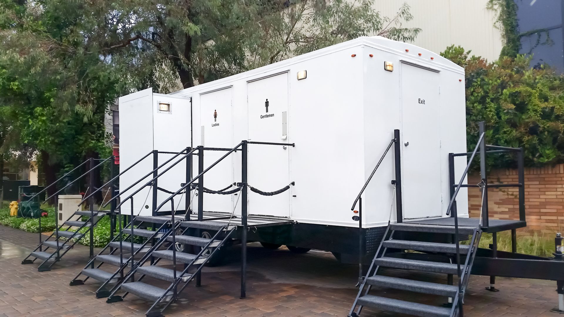 White portable restroom trailer with stair access, parked outdoors.