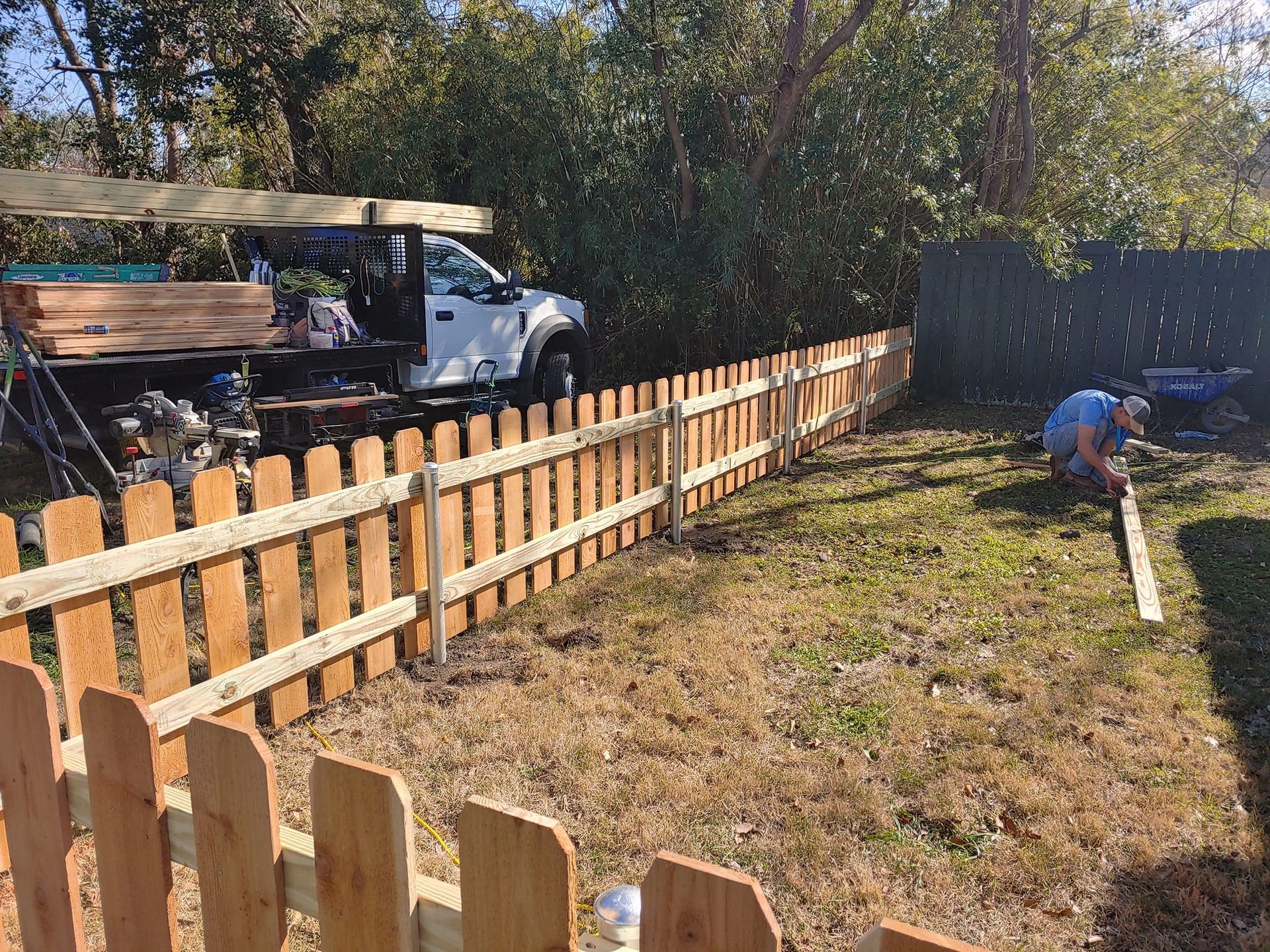 A man is working on a wooden fence in a backyard.