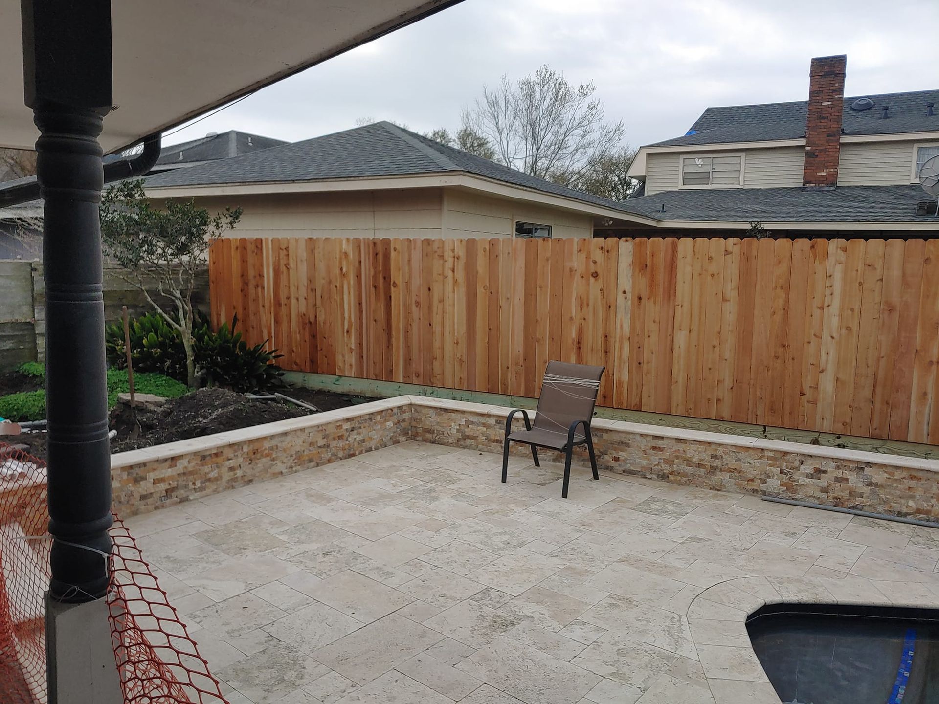 A wooden fence surrounds a patio with a chair and a pool.