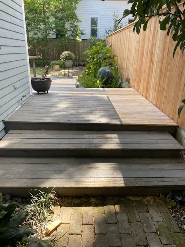 A wooden deck with stairs leading up to it next to a wooden fence.
