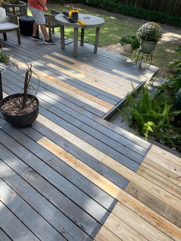 A man is standing on a wooden deck with a table and chairs.