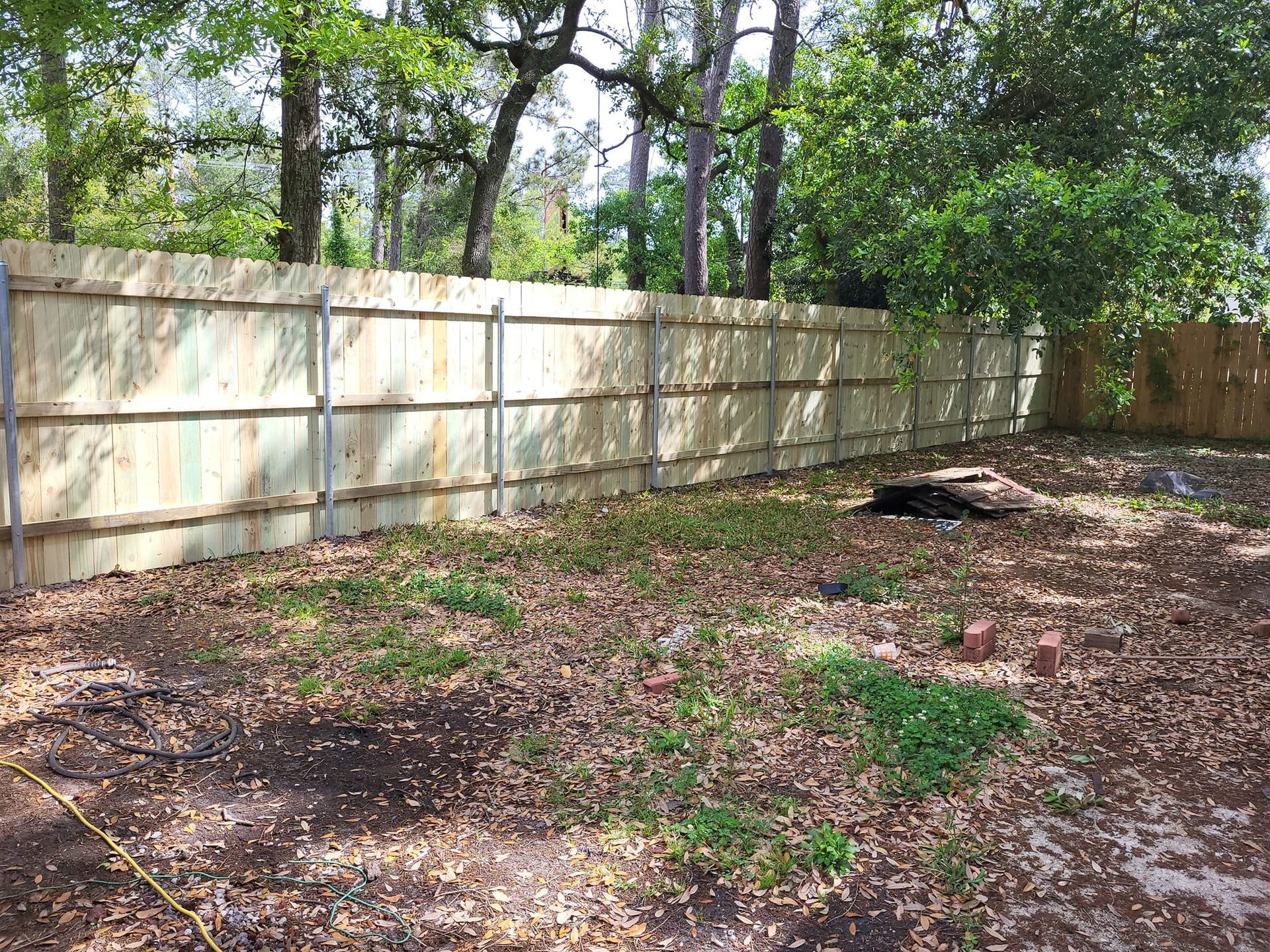A wooden fence is surrounded by trees in a backyard.