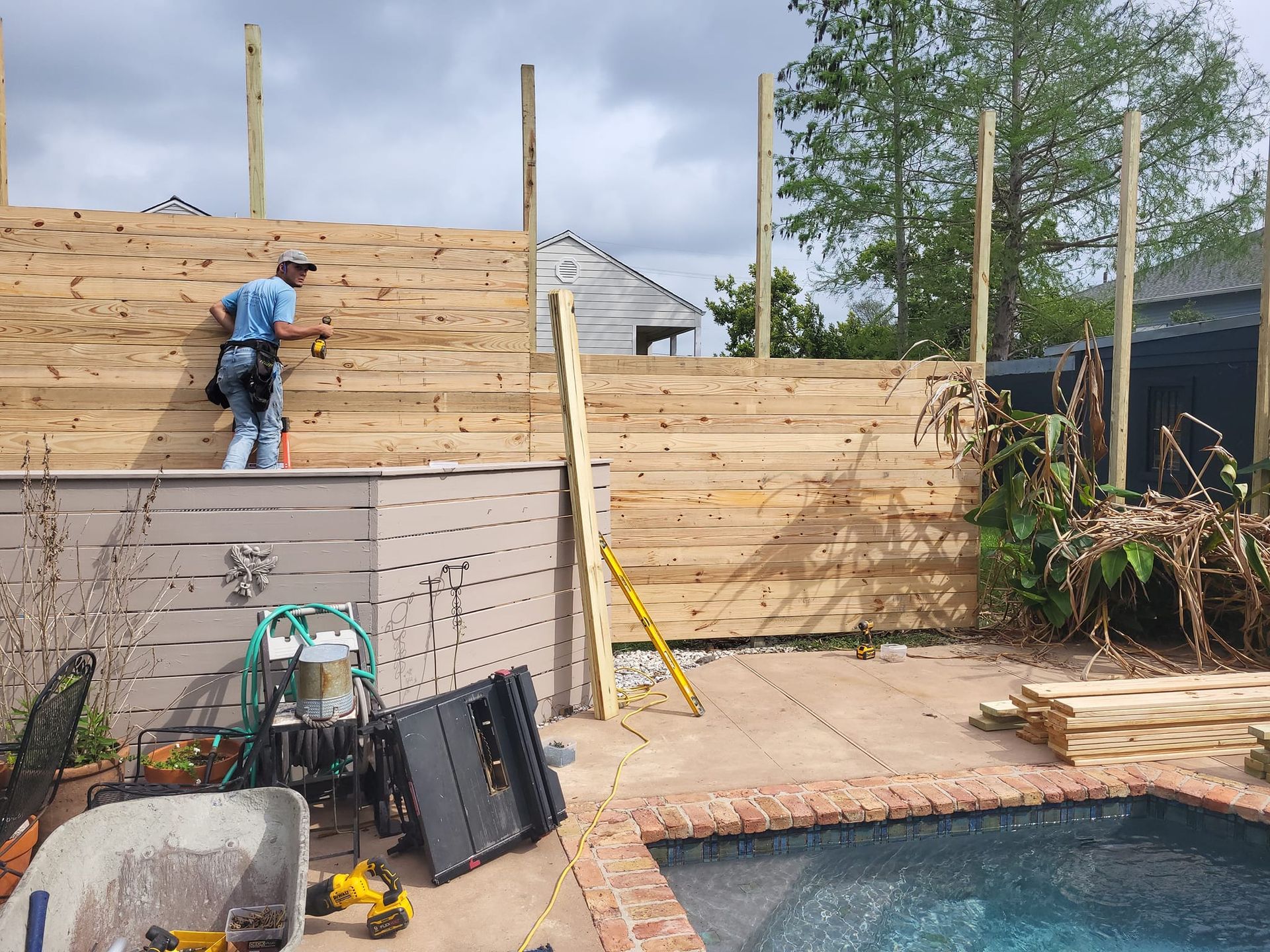 A man is working on a wooden fence next to a pool.