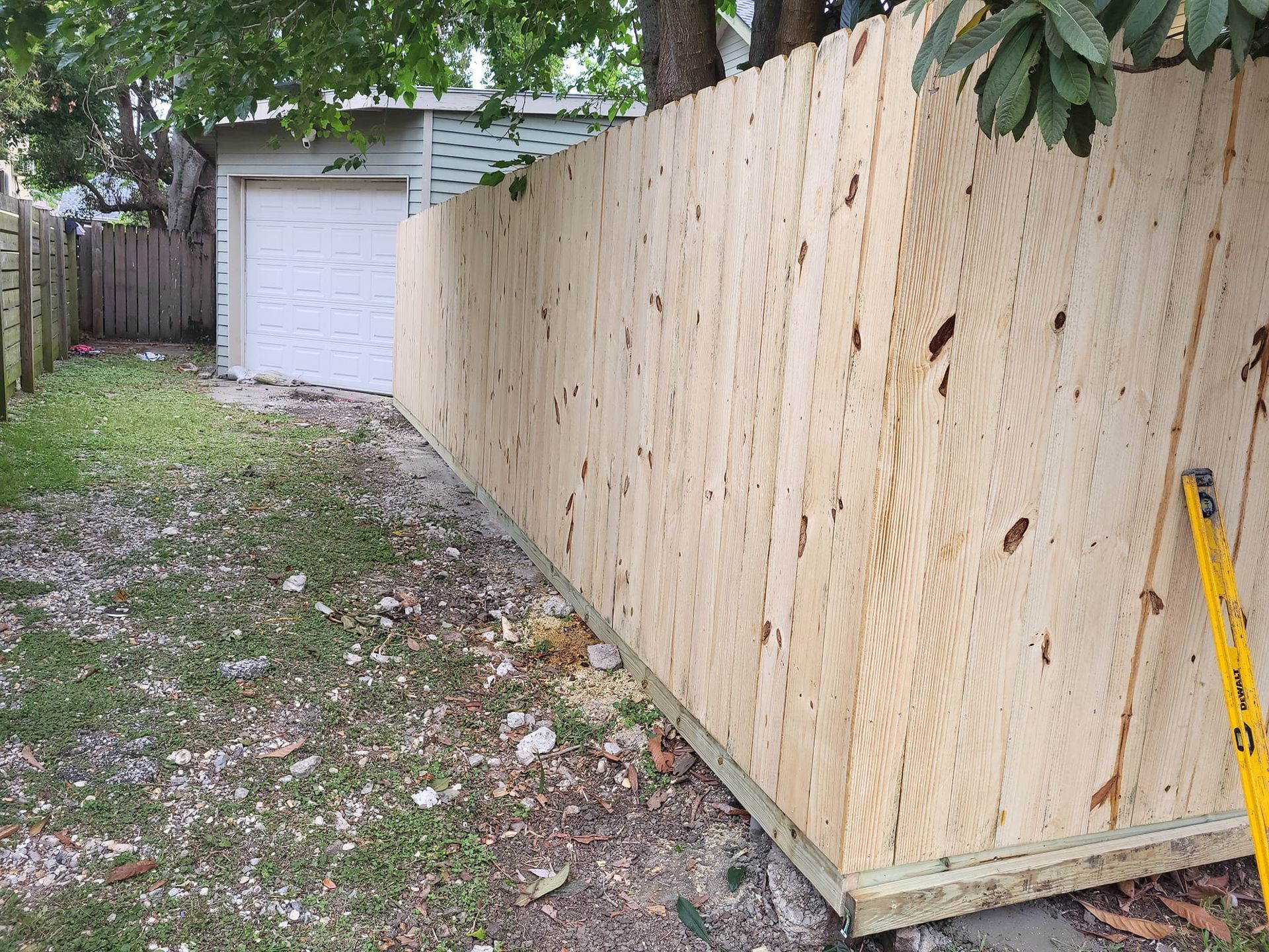 A wooden fence is being built in a backyard next to a garage.