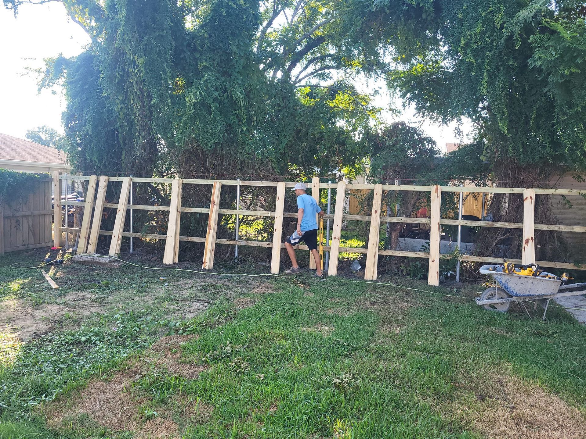 A man is standing next to a wooden fence in a backyard.