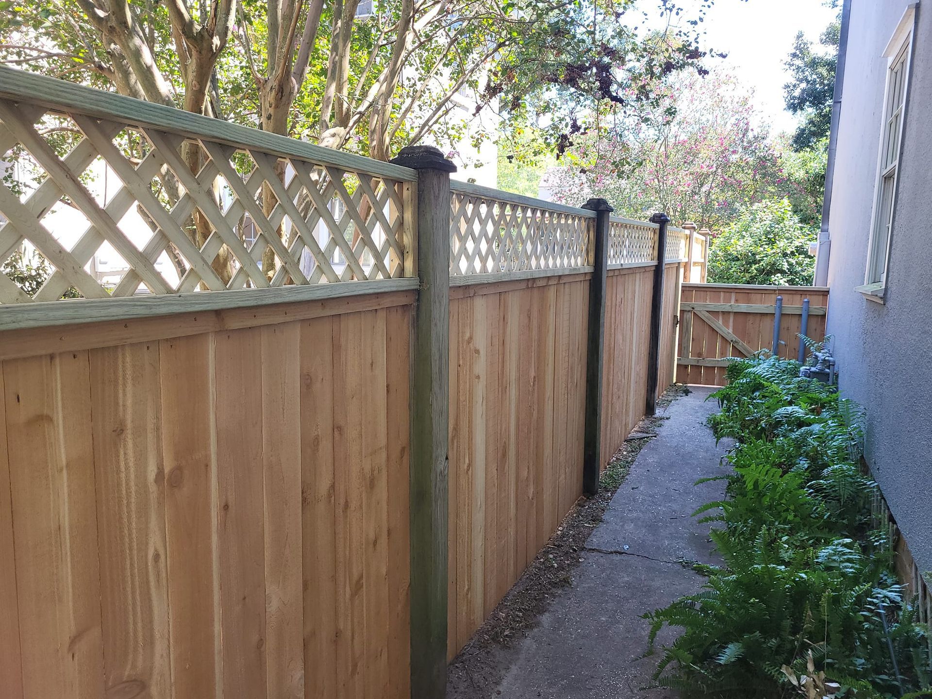 A wooden fence with a lattice on it is next to a sidewalk.