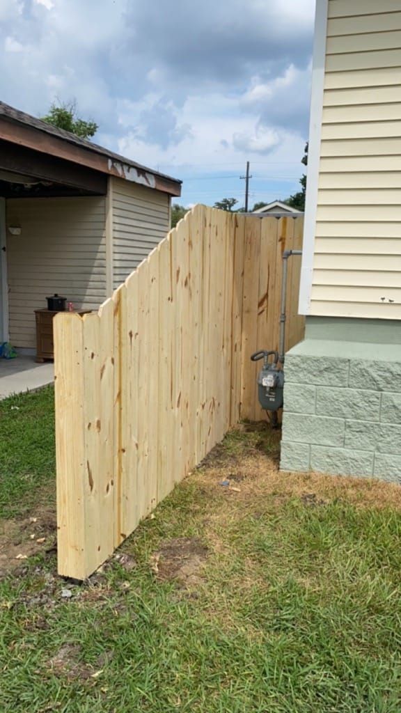 A wooden fence is sitting in the grass next to a house.
