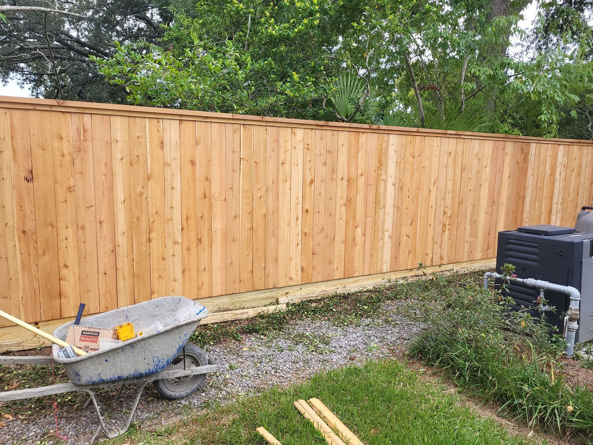 A wooden fence is being built in a backyard with a wheelbarrow in front of it.