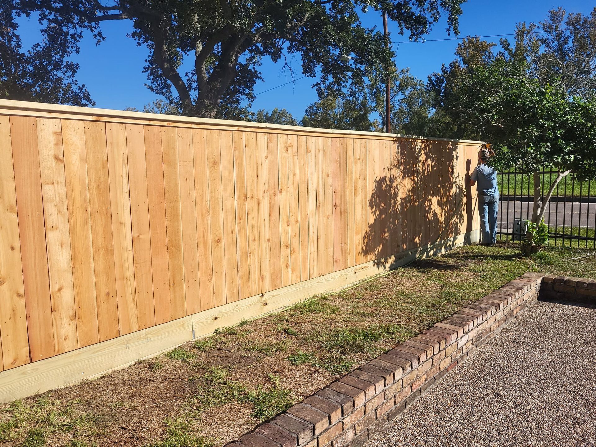 A man is standing next to a wooden fence in a yard.