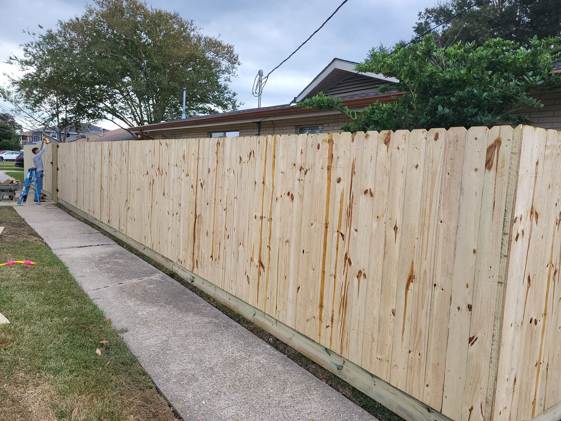 A wooden fence is being built next to a sidewalk.