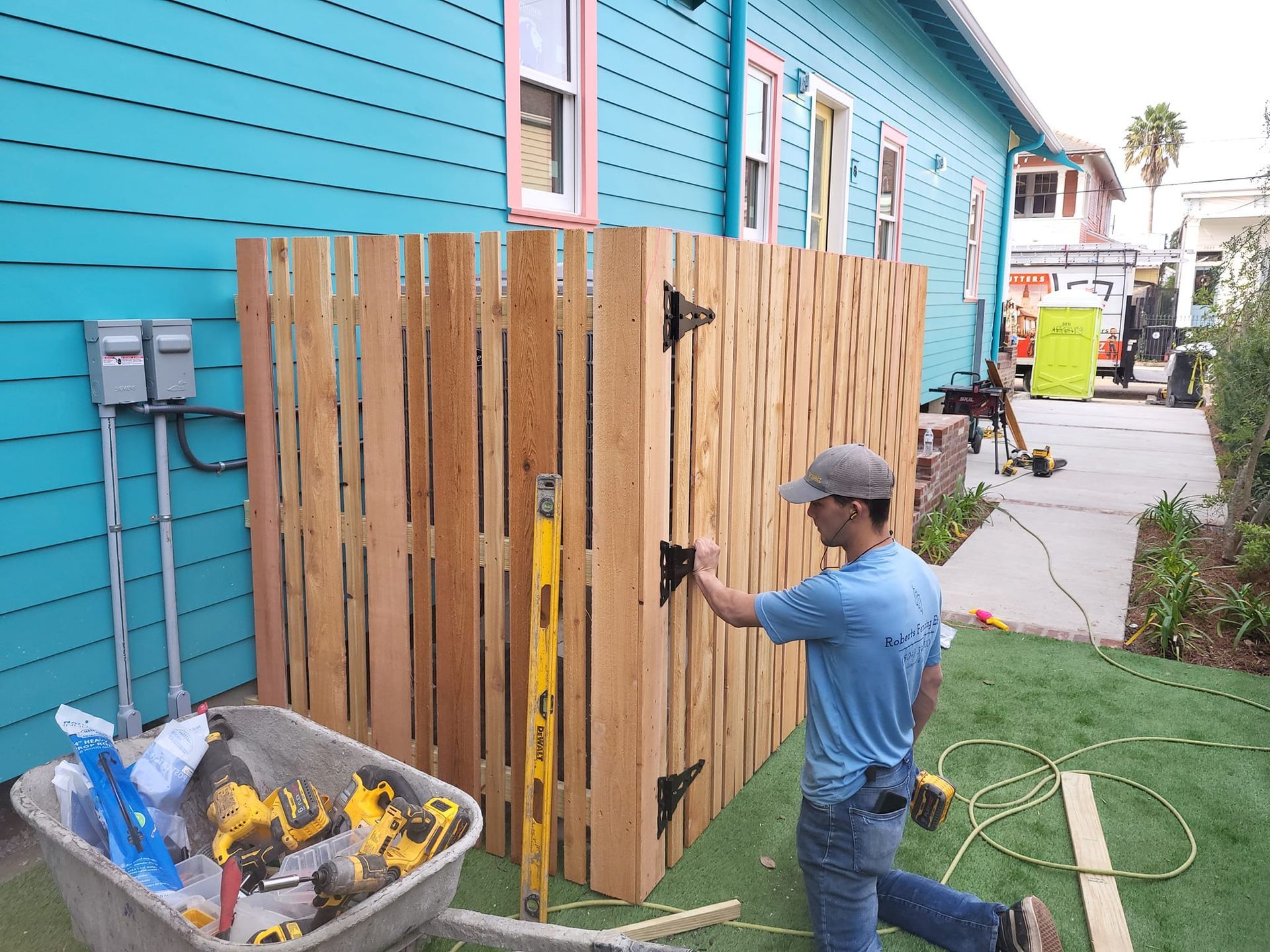A man is working on a wooden fence in front of a blue house.