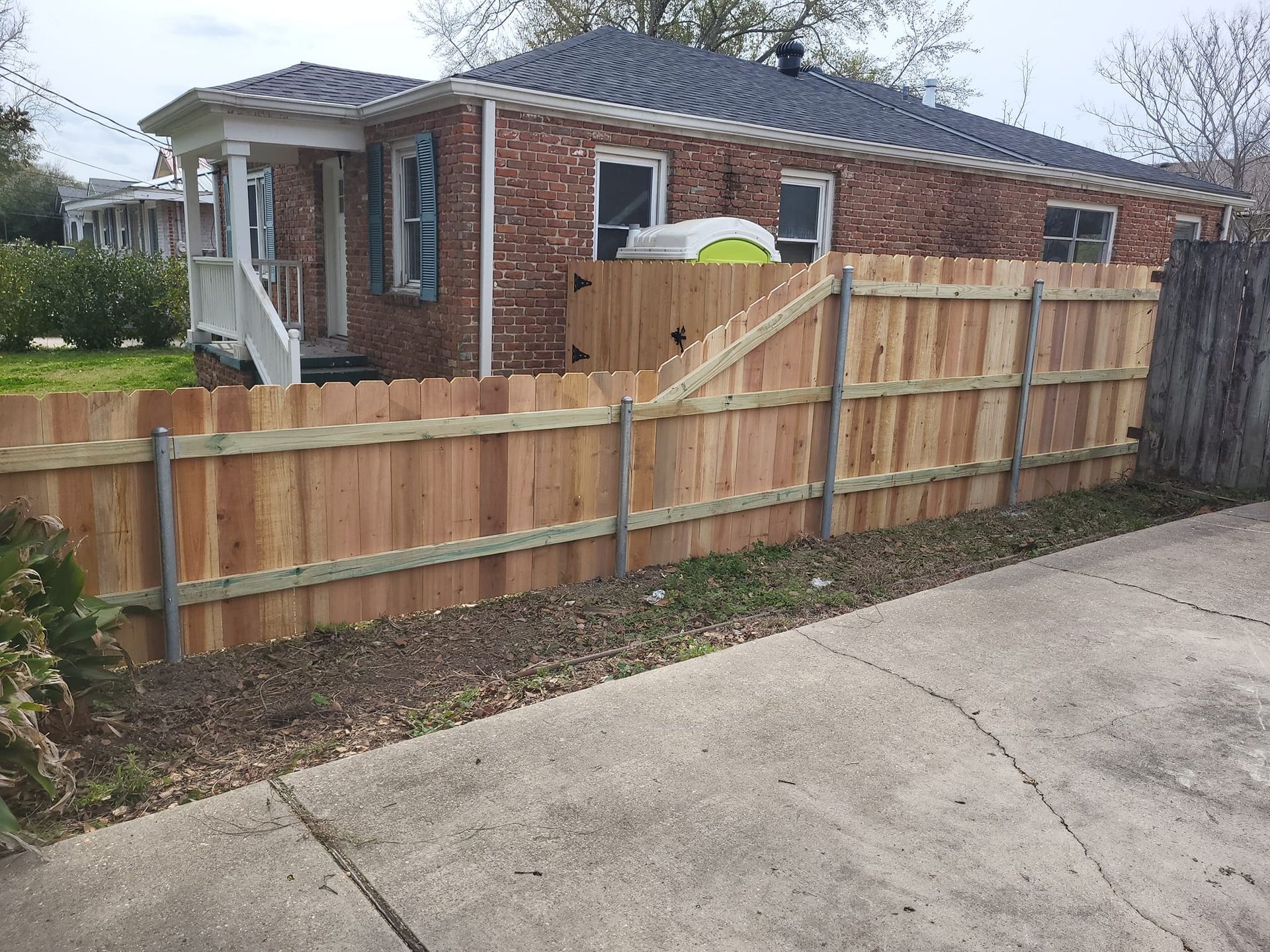 A wooden fence is in front of a brick house.