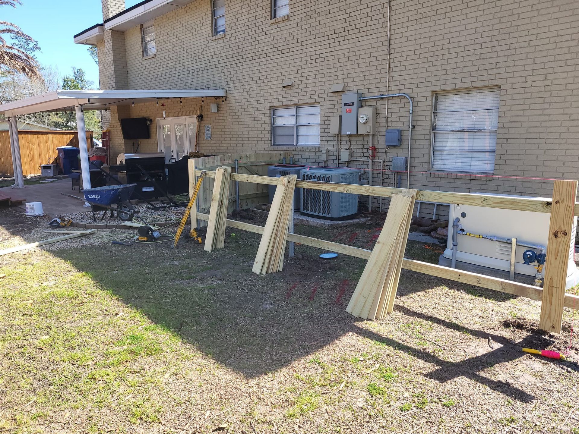 A wooden fence is being built in the backyard of a house.