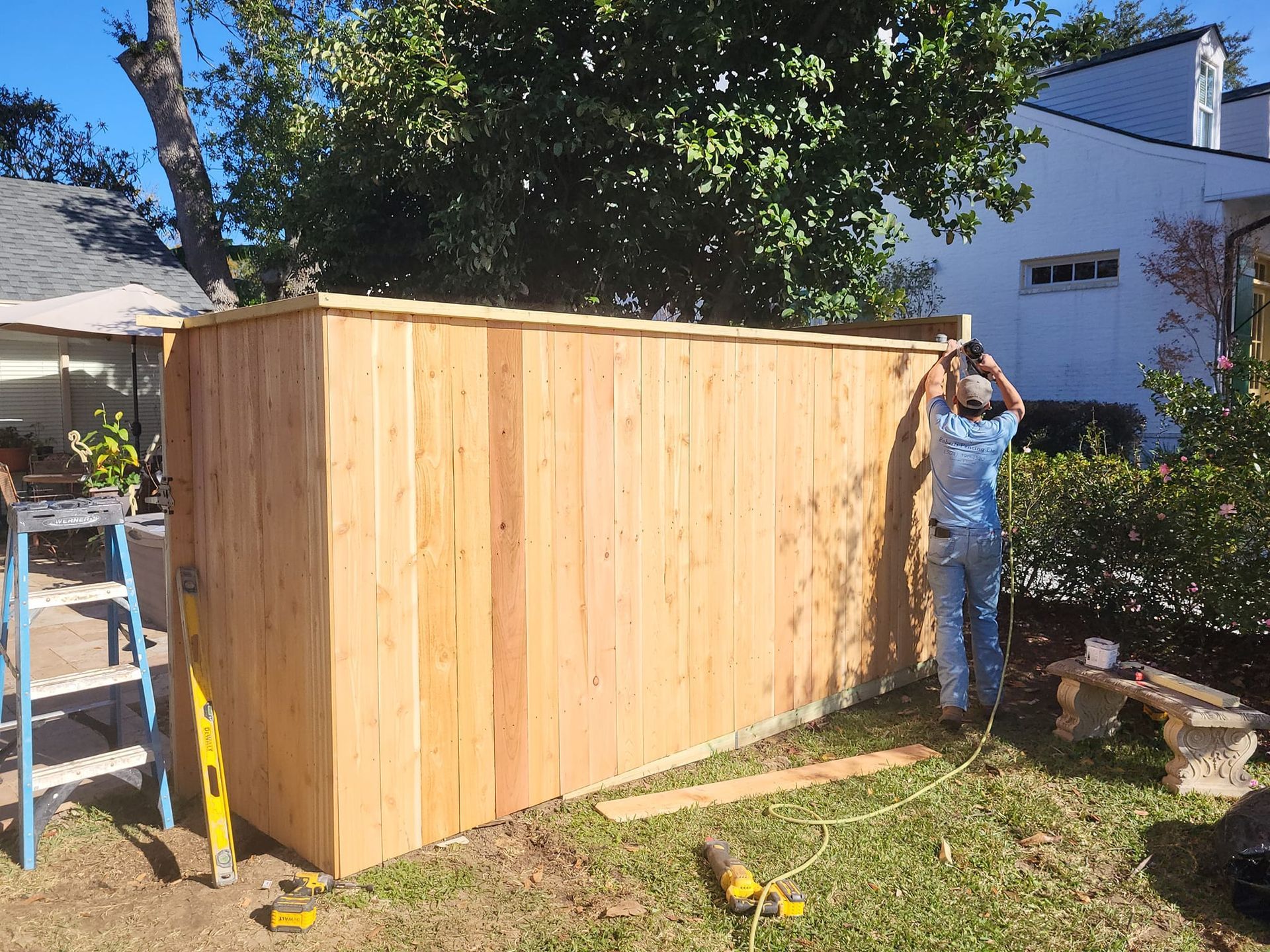 A man is standing next to a wooden fence in a yard.