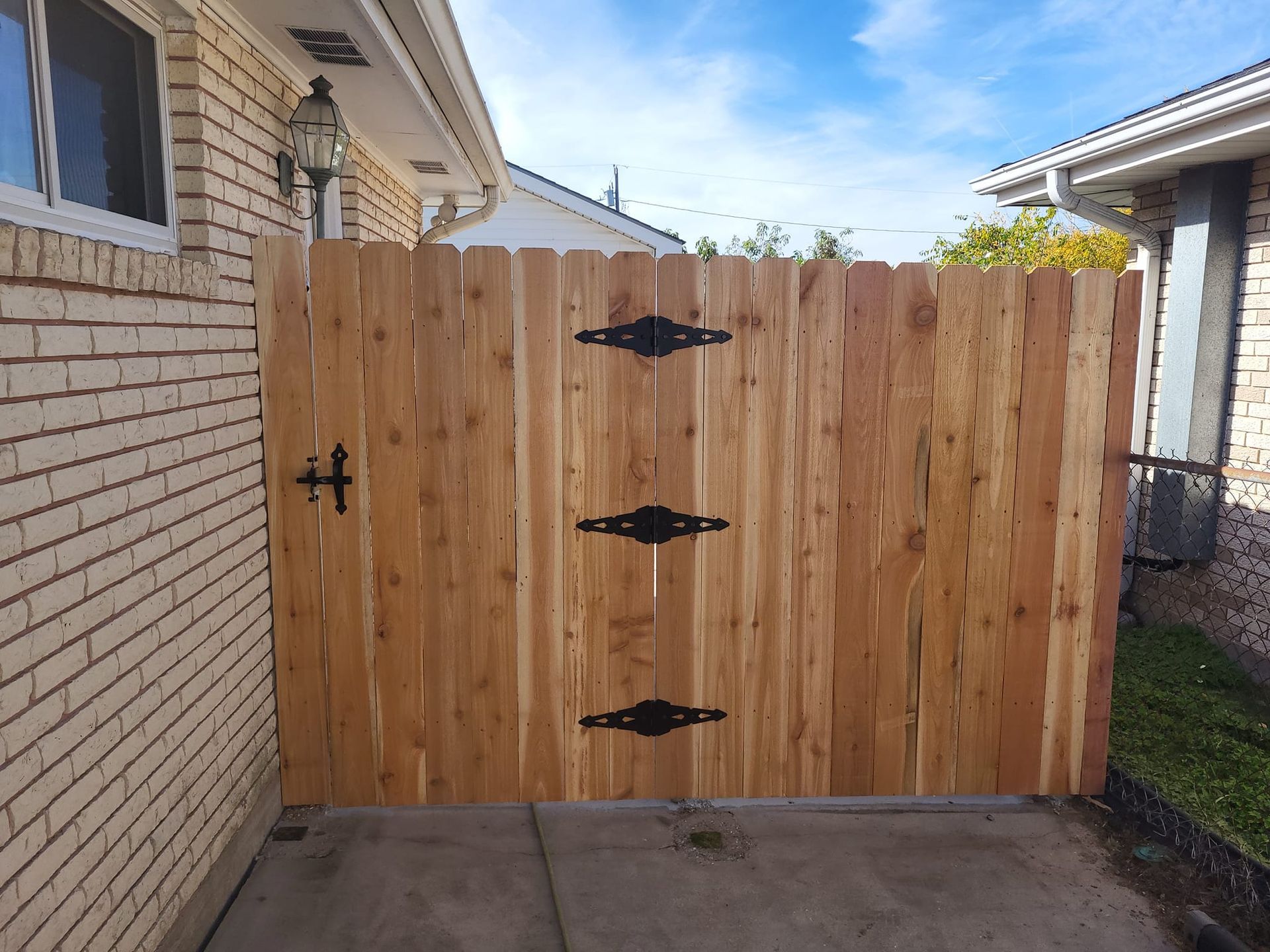 A wooden fence with black hinges is sitting in front of a brick house.