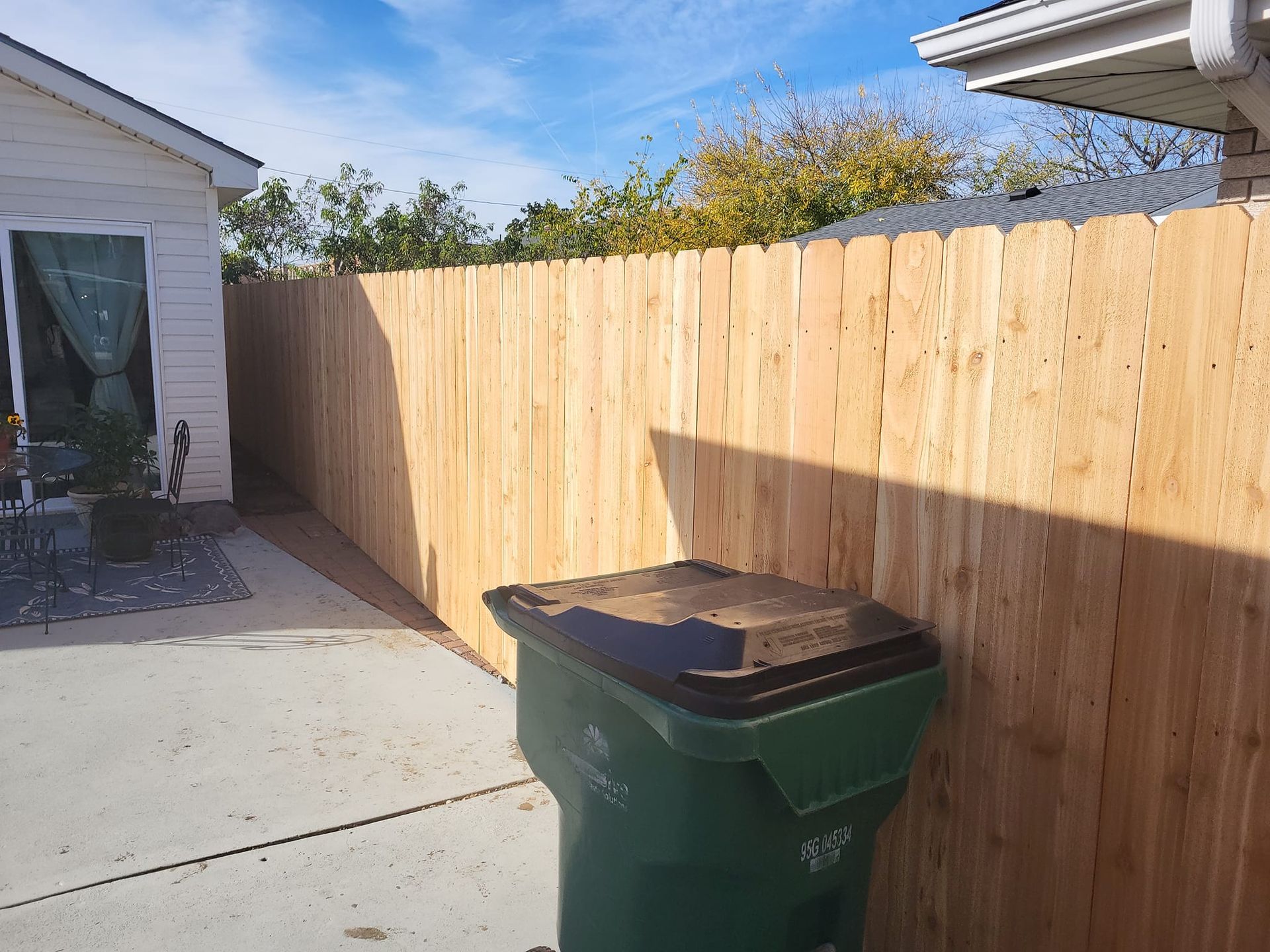 A wooden fence with a green trash can in front of it.