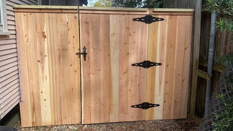A wooden fence with black hinges is sitting next to a house.