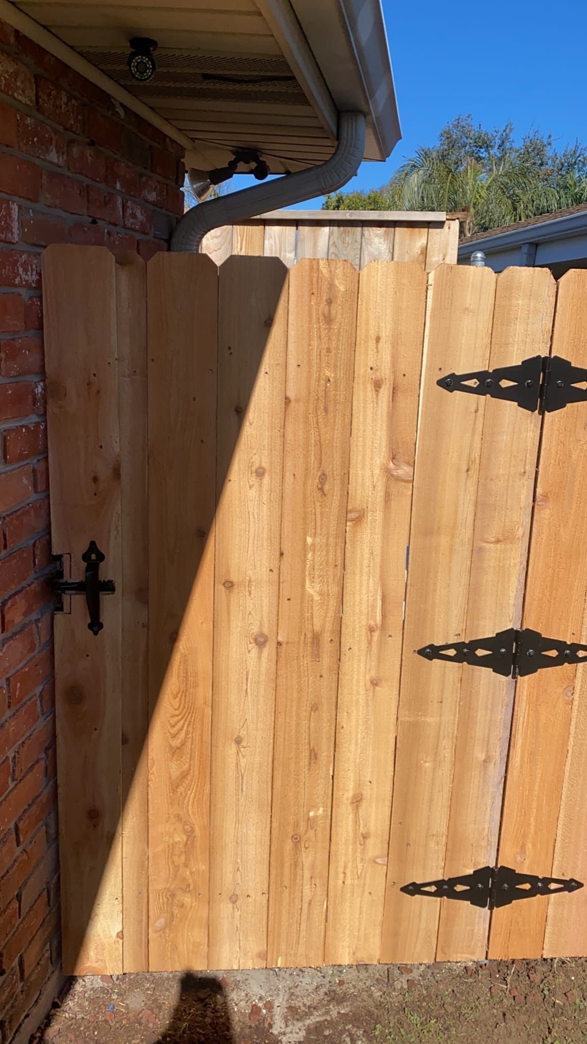 A wooden fence with black hinges is attached to a brick wall.