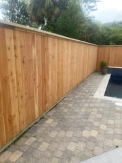A wooden fence surrounds a swimming pool in a backyard.
