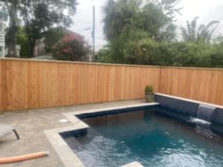 A wooden fence surrounds a large swimming pool.