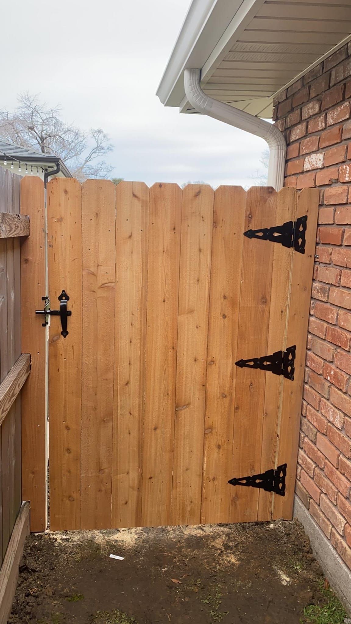A wooden gate with black hinges is sitting next to a brick wall.