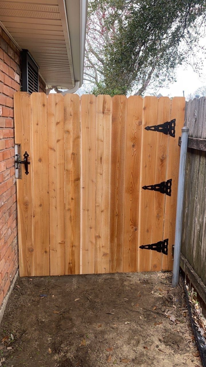 A wooden gate with black hinges is sitting next to a brick wall.