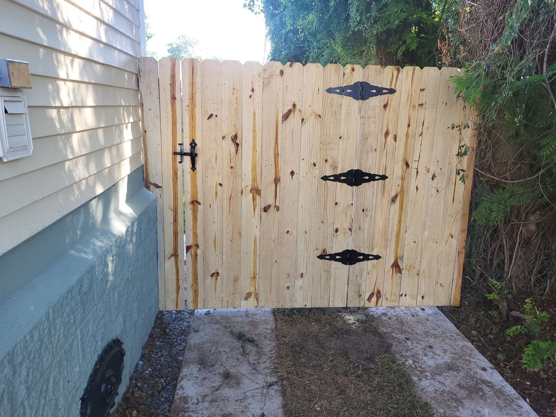 A wooden gate with black hinges is next to a house