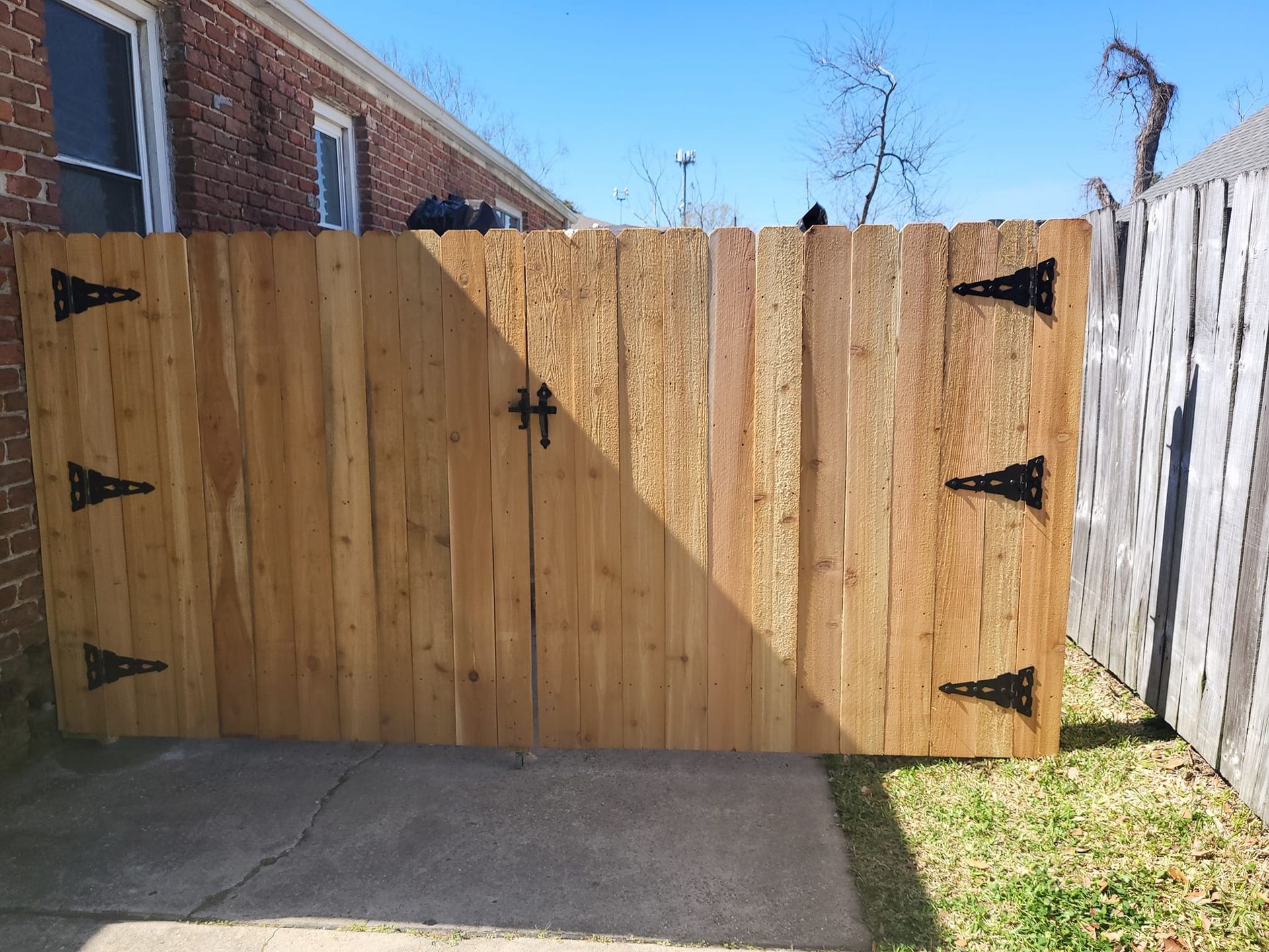 A wooden fence with black hinges is in front of a brick house.