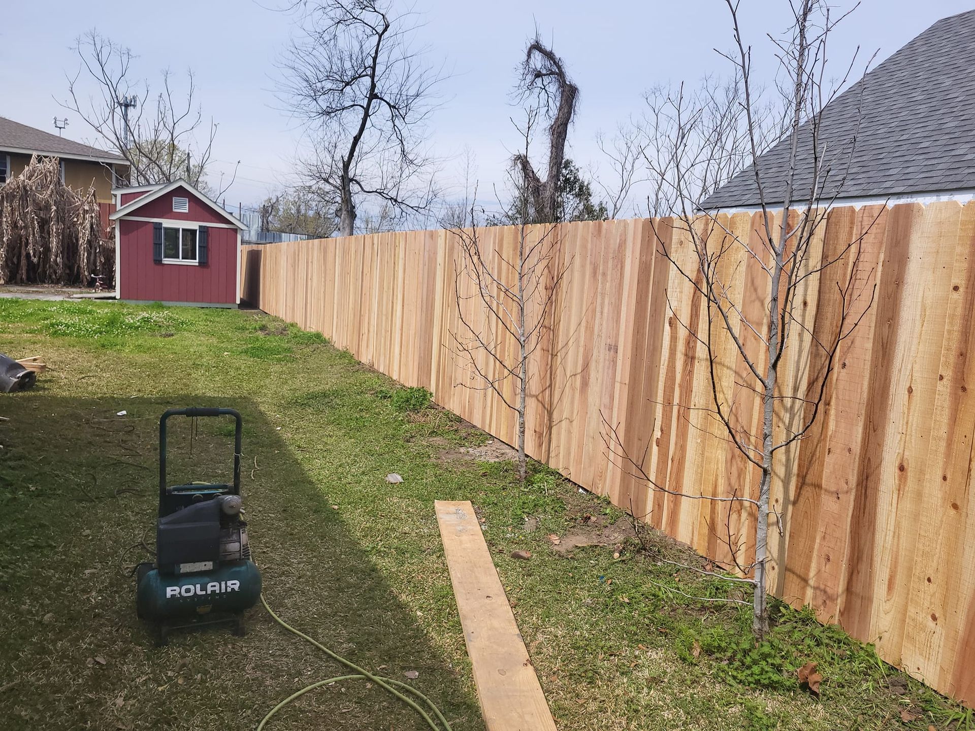 A small air compressor is sitting next to a wooden fence.