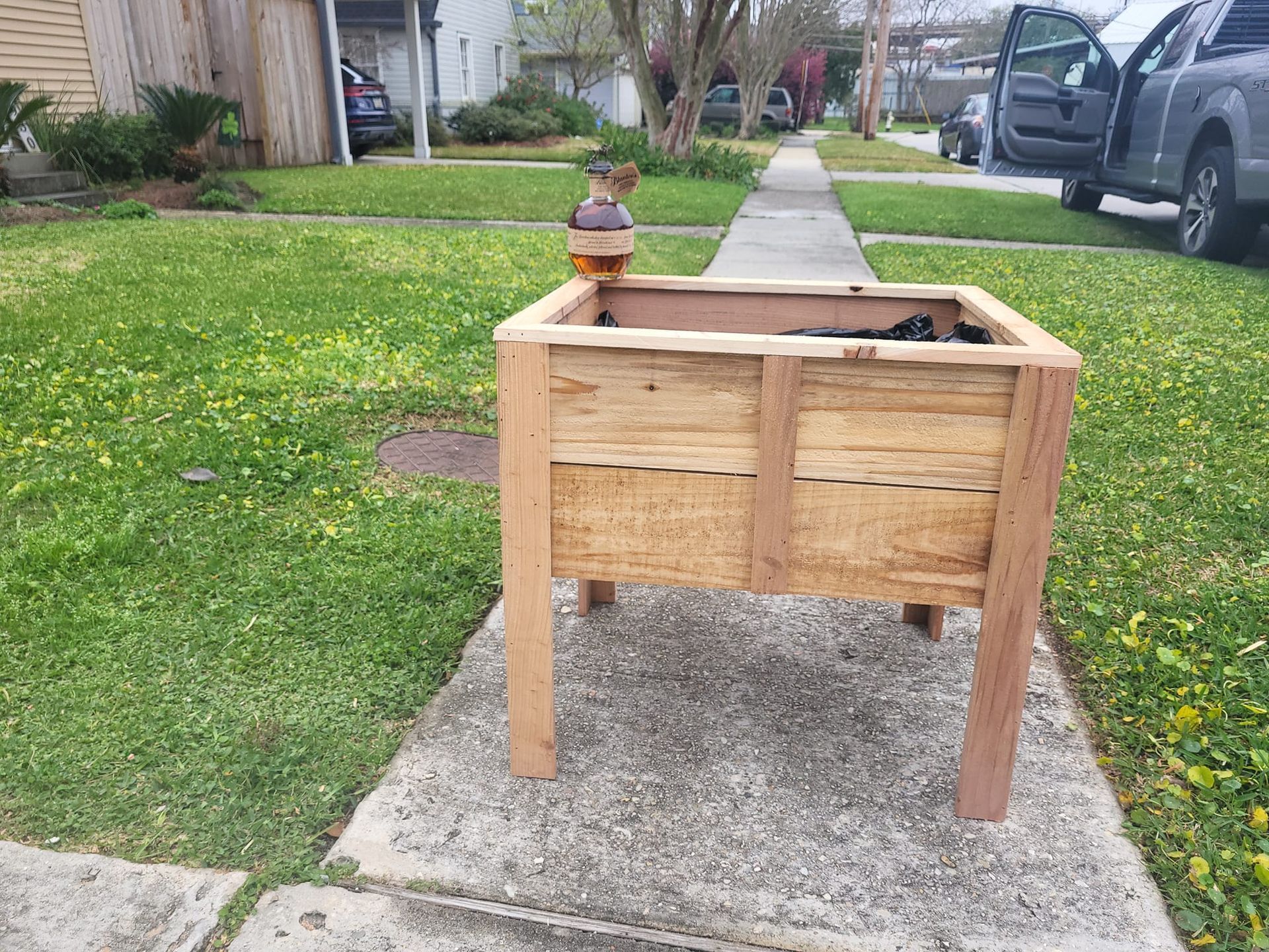 A wooden planter is sitting on a sidewalk in front of a house.