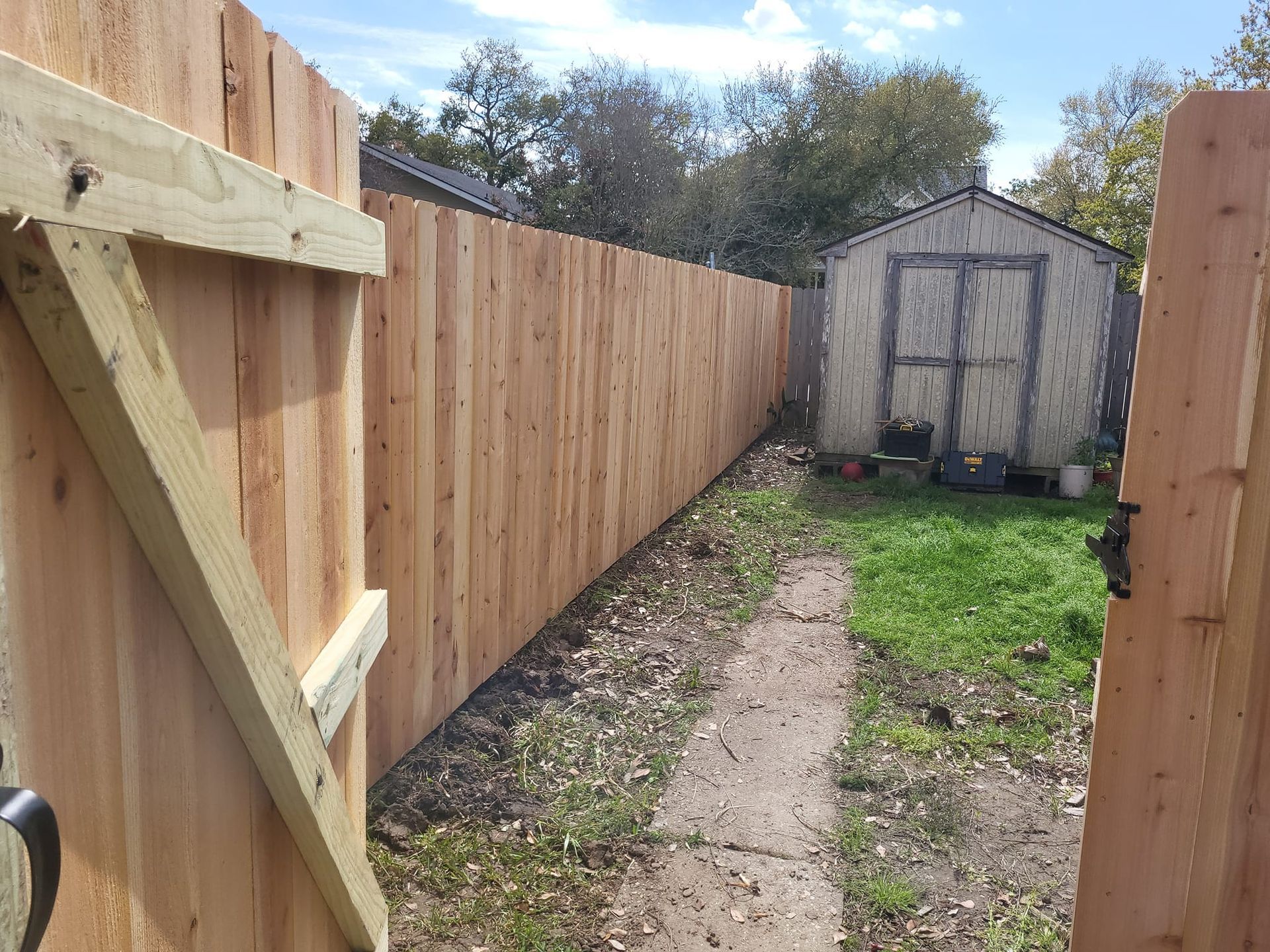 A wooden fence surrounds a dirt path leading to a shed.