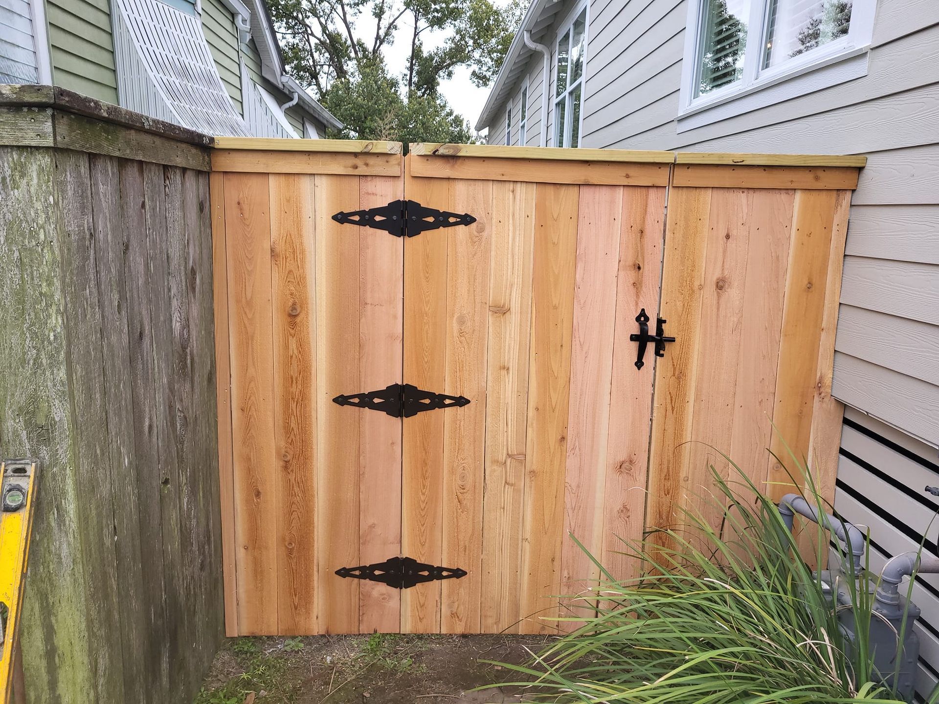 A wooden gate with black hinges is next to a house.