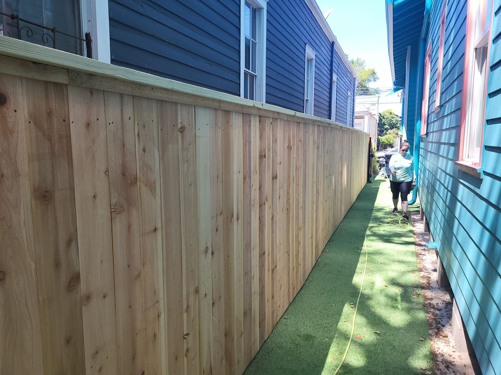 A wooden fence is along the side of a blue house.