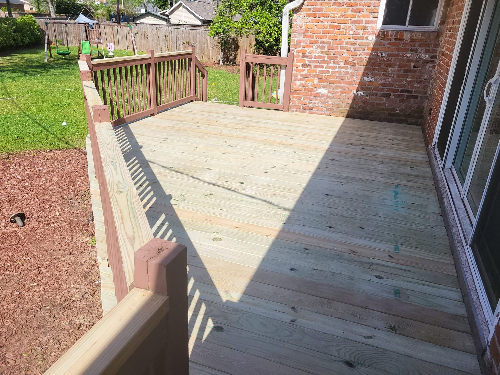 A wooden deck with a railing in front of a brick house.