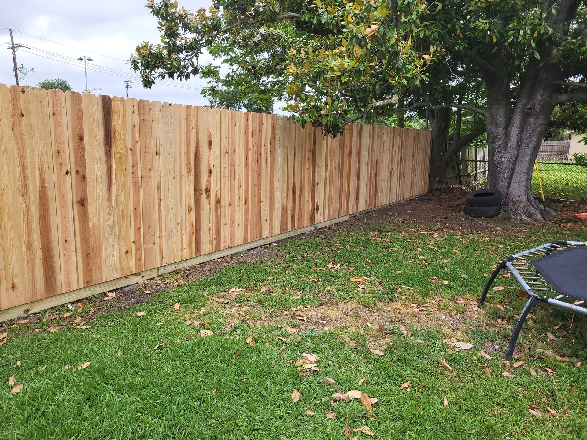 A wooden fence is surrounding a trampoline in a backyard.