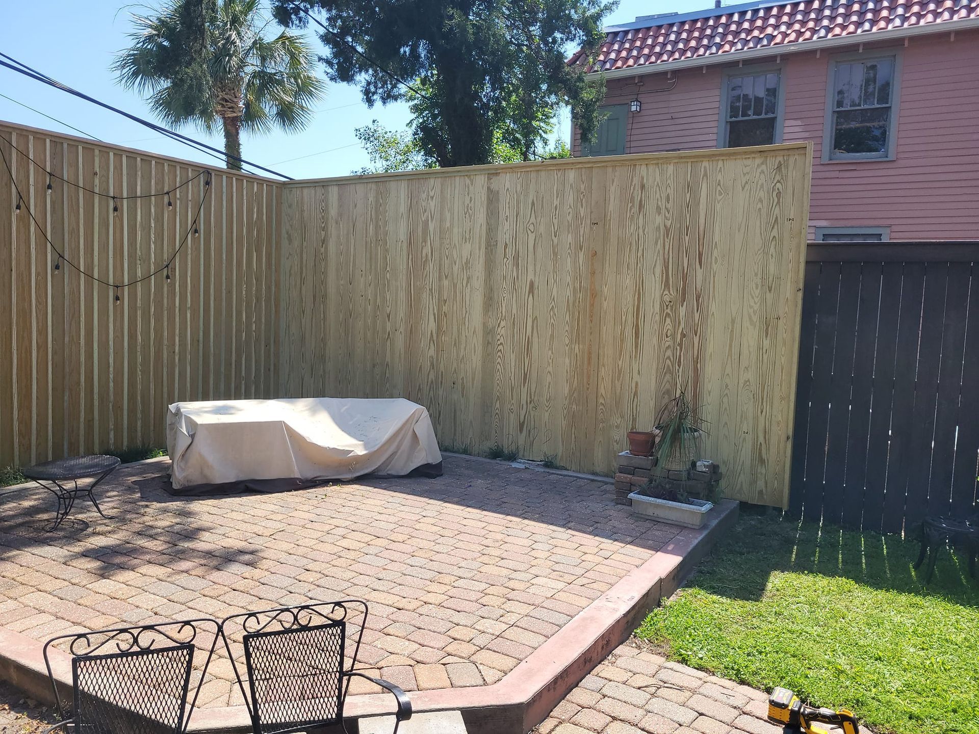 A wooden fence surrounds a patio with a table and chairs.
