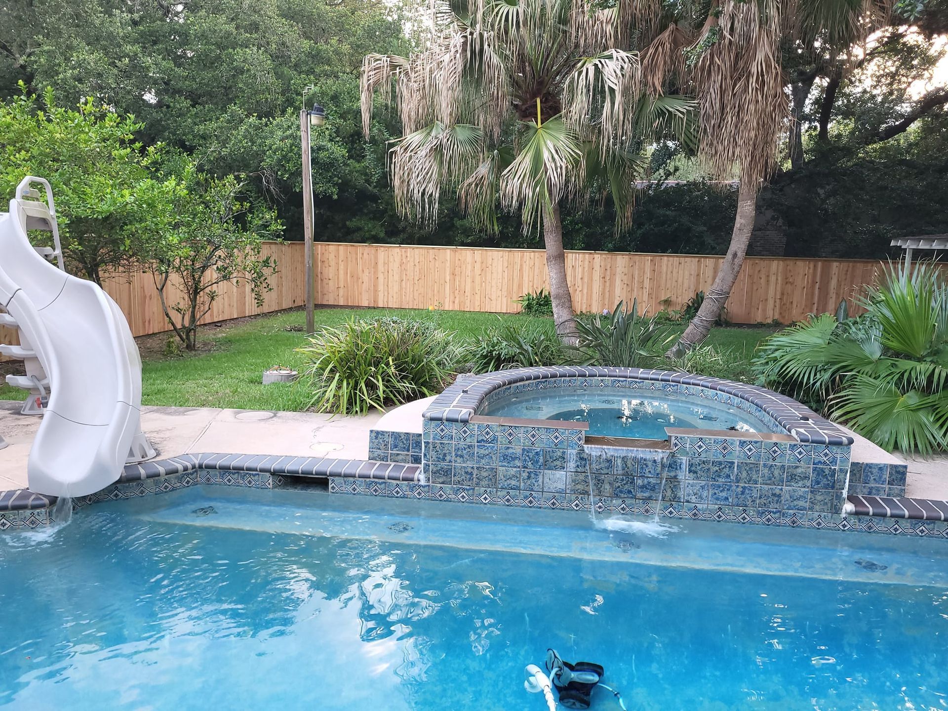 A swimming pool with a slide and a hot tub in the backyard.