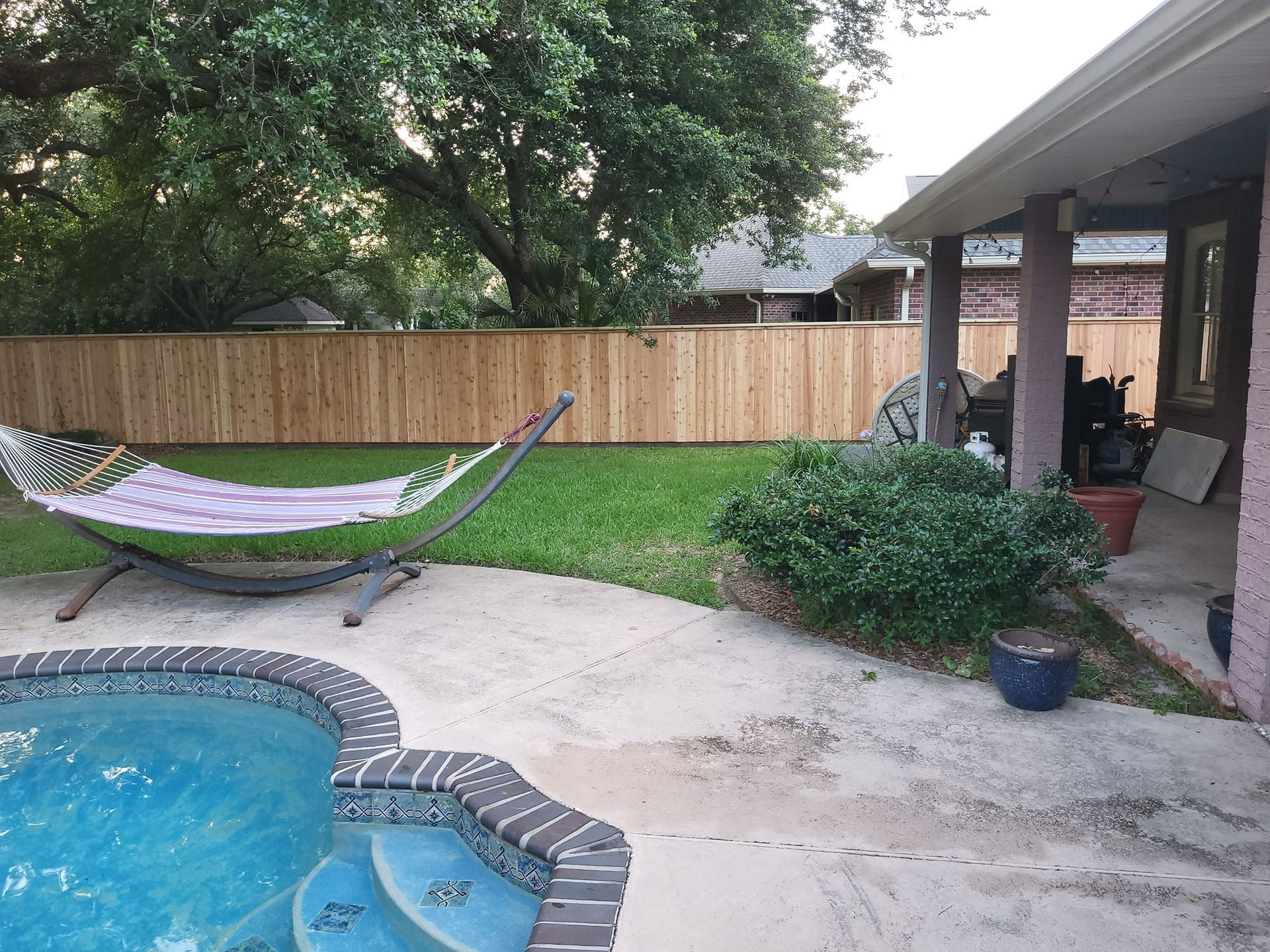 A hammock is sitting next to a pool in a backyard